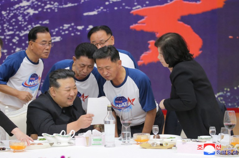 Kim, sentada en una mesa de banquete, mirando un trozo de papel con personas vestidas con camisetas de NATA.
