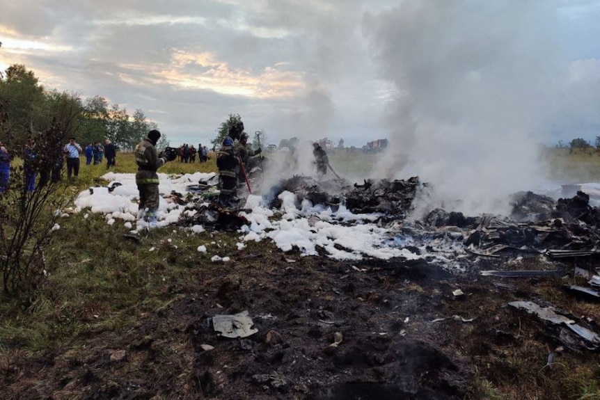 Los restos humeantes de un avión con bomberos alrededor