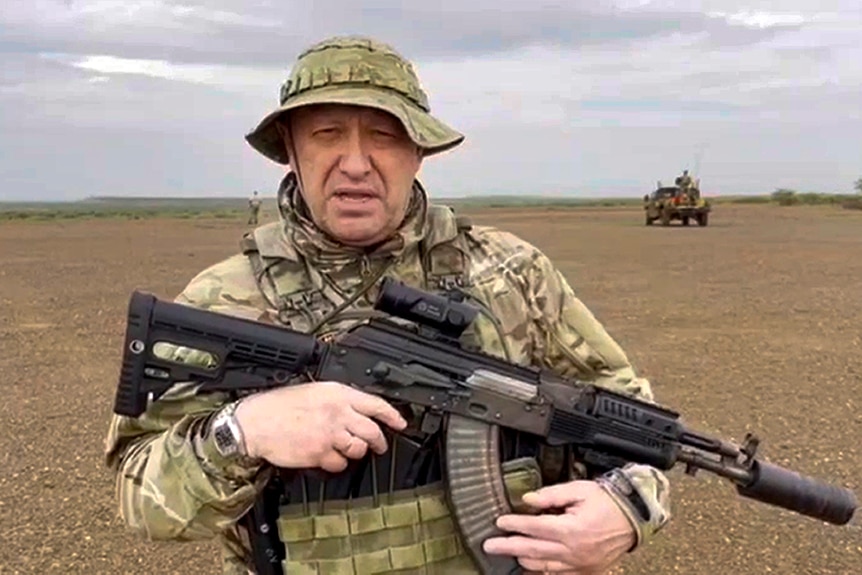 Yevgeny Prigozhin se encuentra en una llanura abierta sosteniendo un arma.