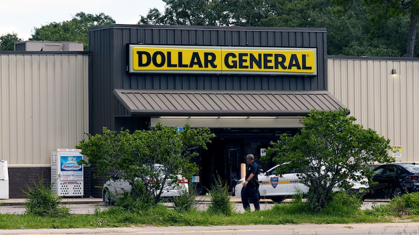 A storefront with a big yellow sign reading dollar general on top with green grass and trees in front and police man and cars