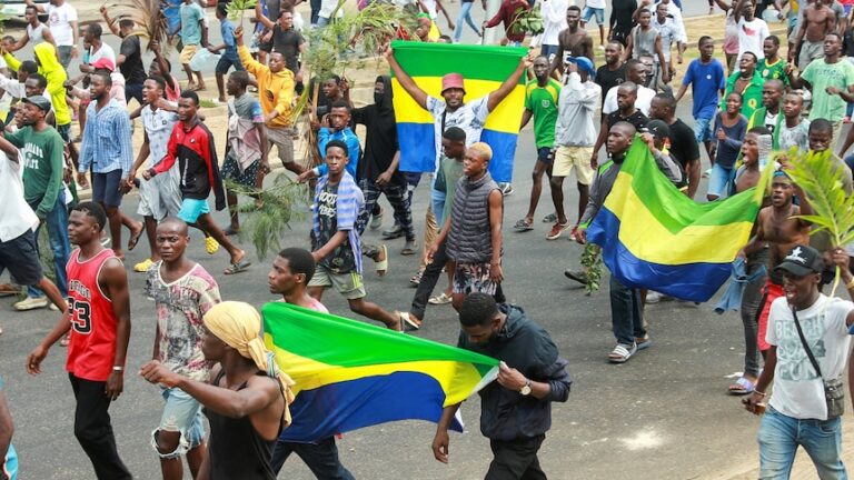 People marching through a street carrying green, yellow, and blue flags