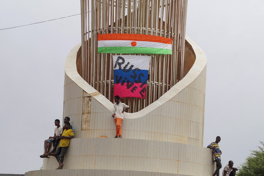 Los hombres se encuentran en lo alto de la estructura frente a las banderas de Níger y Rusia.