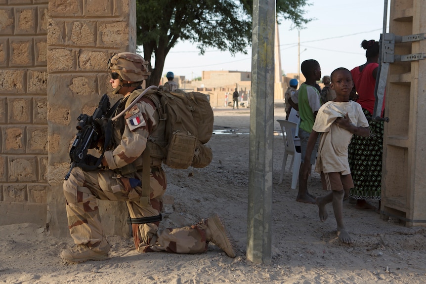 Un soldado francés con un arma se arrodilla mientras pasa un niño maliense.