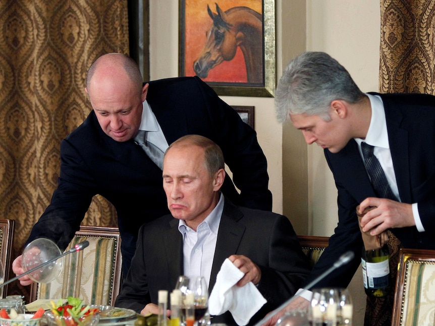 Dos hombres se paran frente al primer ministro ruso, Vladimir Putin, cuando está a punto de empezar a comer.