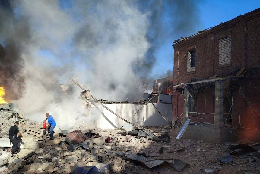Un lugareño intenta apagar edificios en llamas en el lugar de un ataque con misiles rusos.