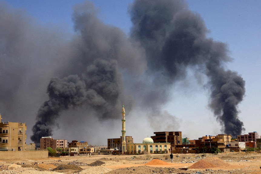     Un hombre camina mientras el humo se eleva sobre los edificios después del bombardeo aéreo
