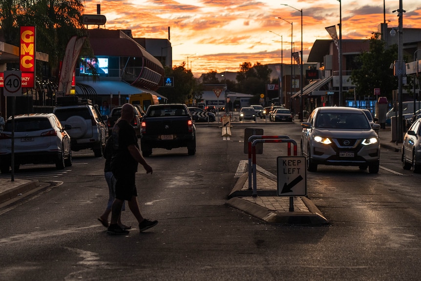 Personas y automóviles en una calle concurrida del distrito financiero de Alice Springs mientras el sol se pone en el horizonte. 