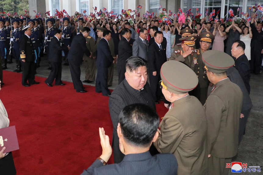 Kim Jong Un y funcionarios se dan la mano en la alfombra roja. 