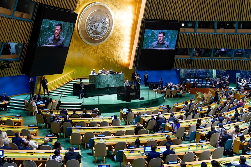 Sala de la ONU con Zelenskyy hablando proyectado en dos pantallas en el escenario. 