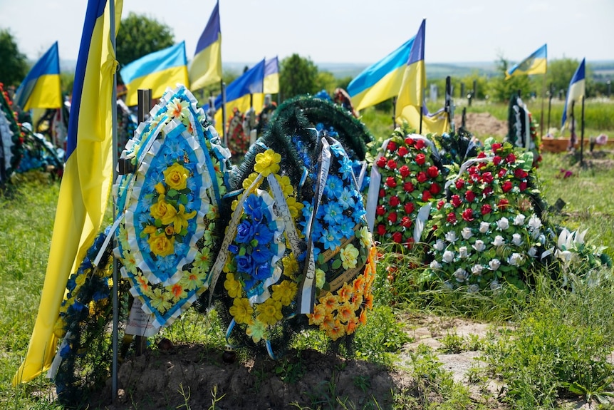 Banderas y flores en varias tumbas de un cementerio.