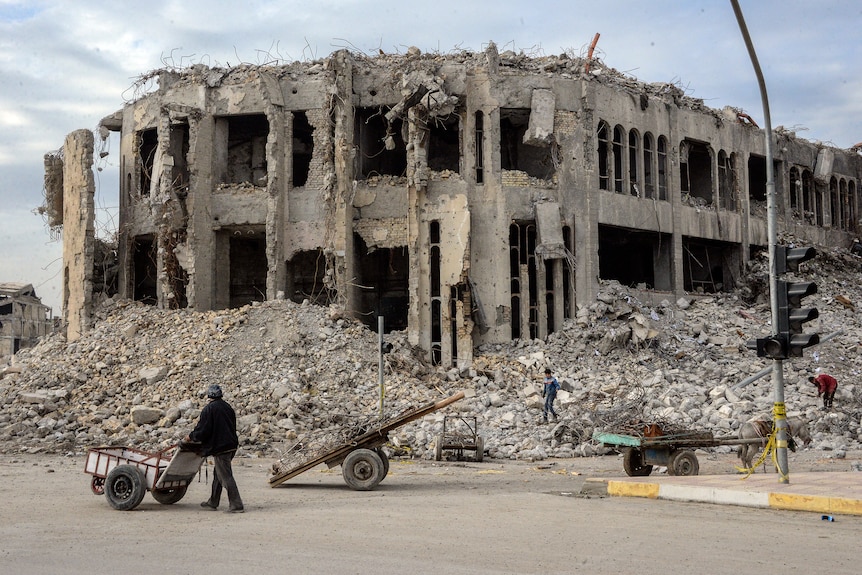 Un iraquí empuja su carrito entre los escombros del destruido edificio Chadirji de siete pisos.