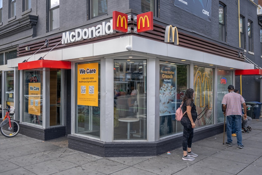 Una tienda McDonalds en un edificio de la esquina, con varias personas reunidas afuera.