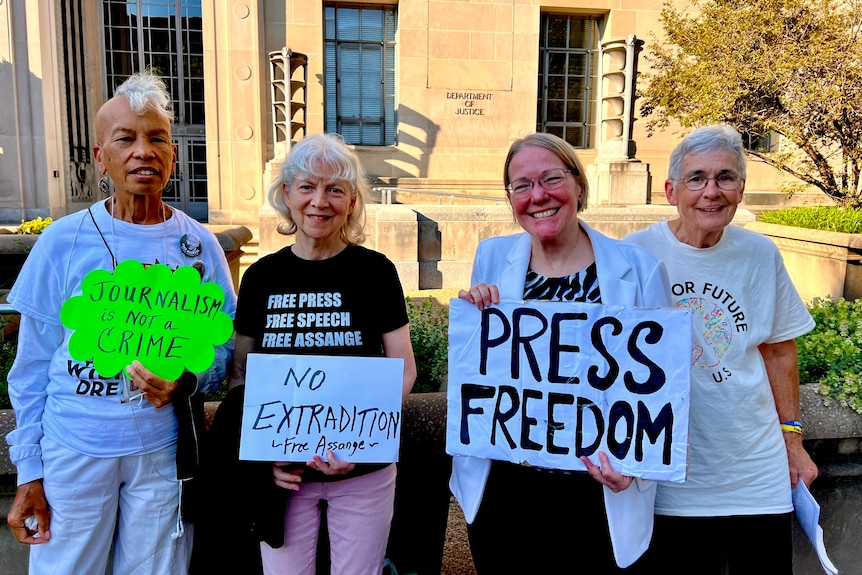 Cuatro mujeres sostienen carteles con mensajes como “libertad de prensa” y “no extradición” frente a un edificio de ladrillo.