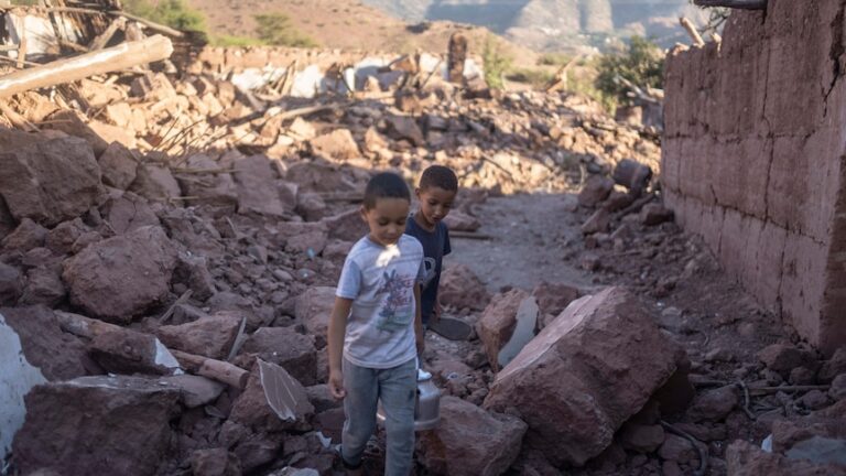 Two boys walk through rubble.