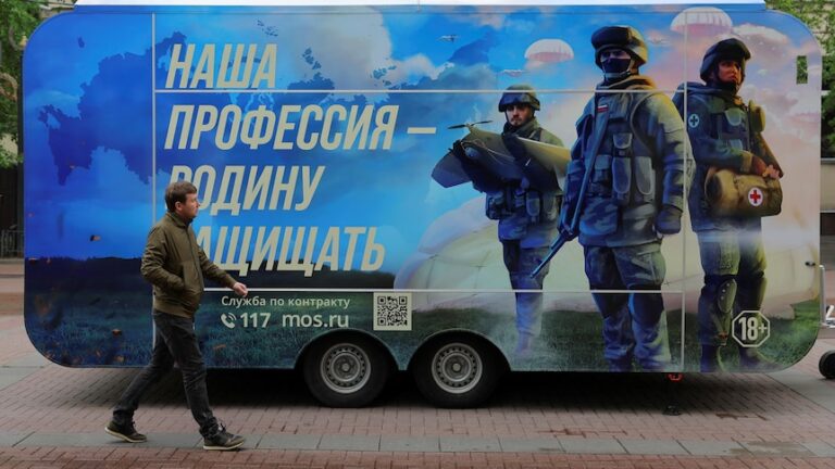 A pedestrian walks past a mobile recruitment point with soldiers painted on the side.