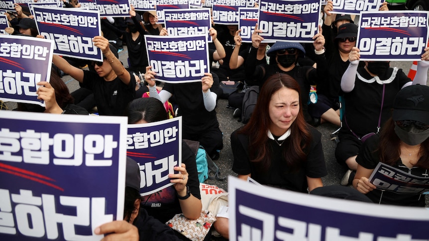 People dressed all in black hold up placards with Korean text.