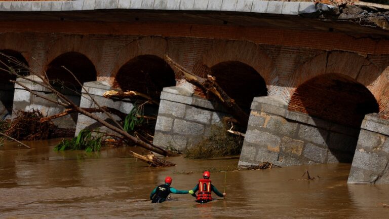 Two people in red hi-vis swim through flood waters next to a bridge.