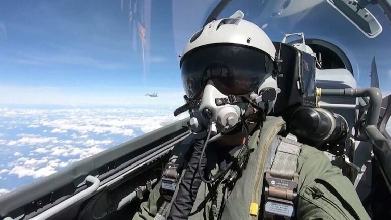 A Chinese air force pilot flies a military jet in full uniform and helmet.