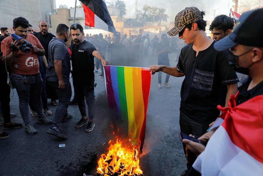 Dos hombres vestidos con una bandera arcoíris lgbt quemada negra 