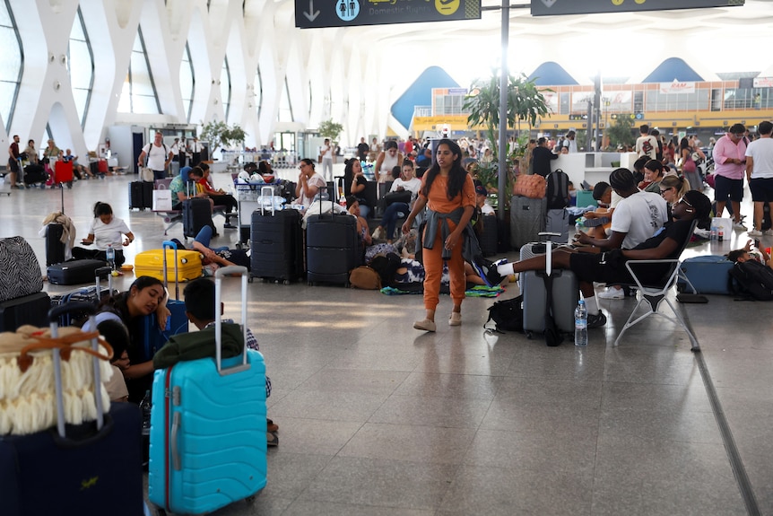 La gente se sienta entre maletas en el suelo de un aeropuerto.