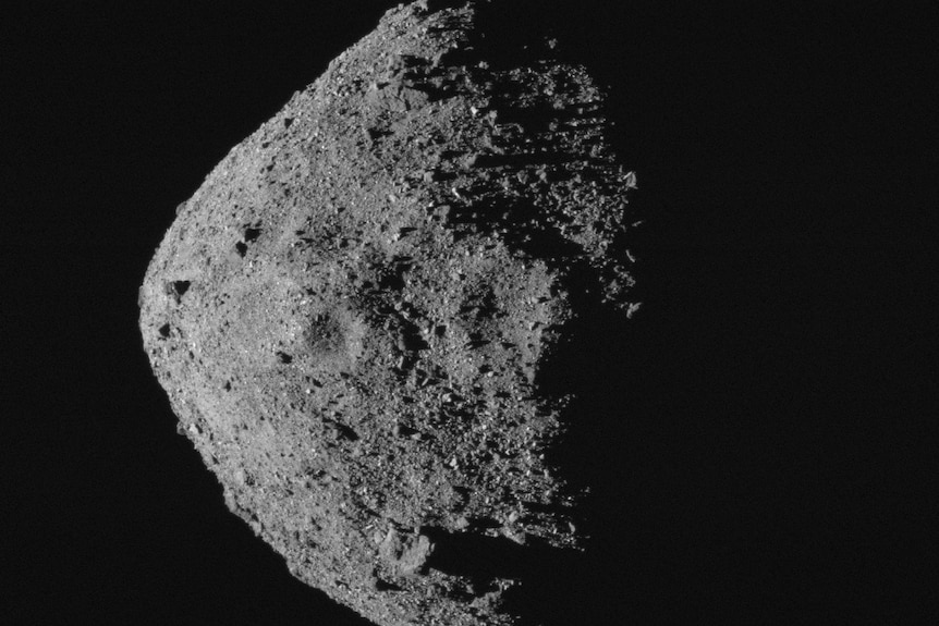 Se ve un asteroide gris emergiendo de la oscuridad del espacio