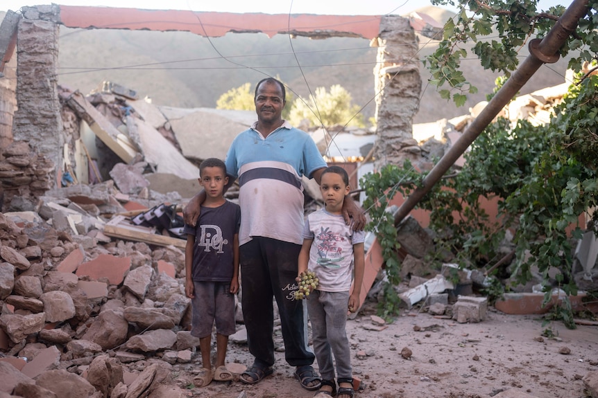 Un padre y sus dos hijos se encuentran entre un montón de escombros.