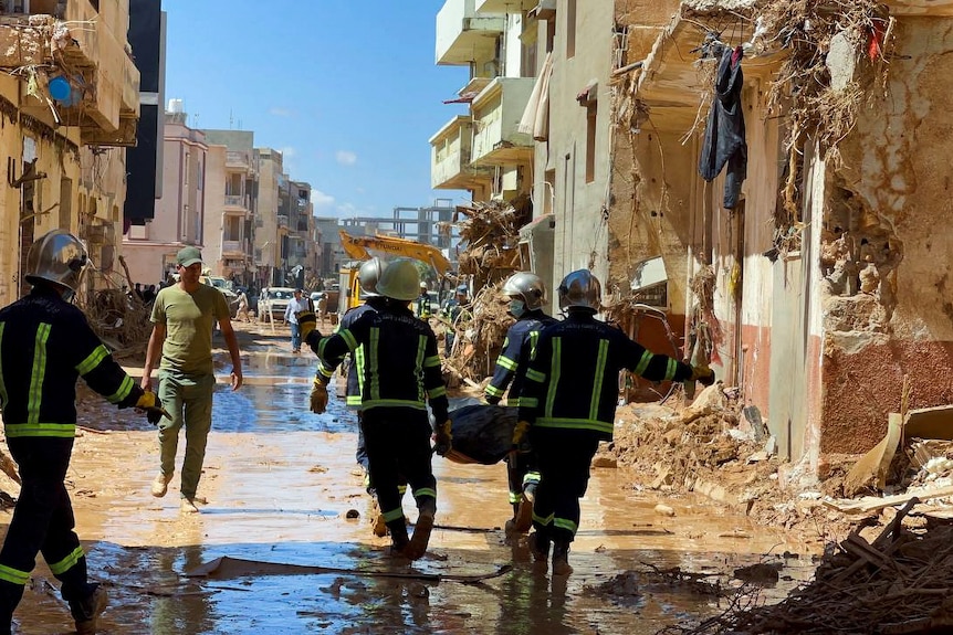 Los rescatistas llevan un cadáver por una calle con edificios destruidos a ambos lados