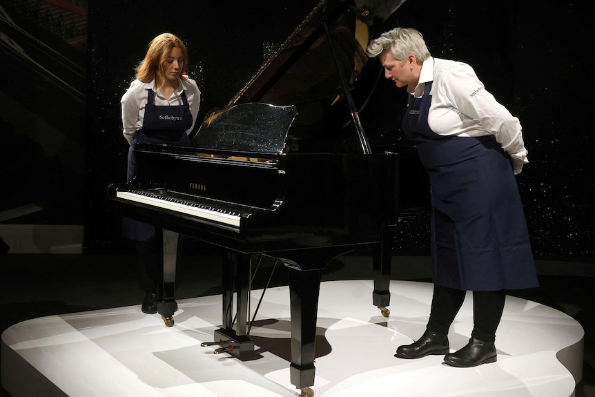 dos personas con delantales miran un piano de cola negro
