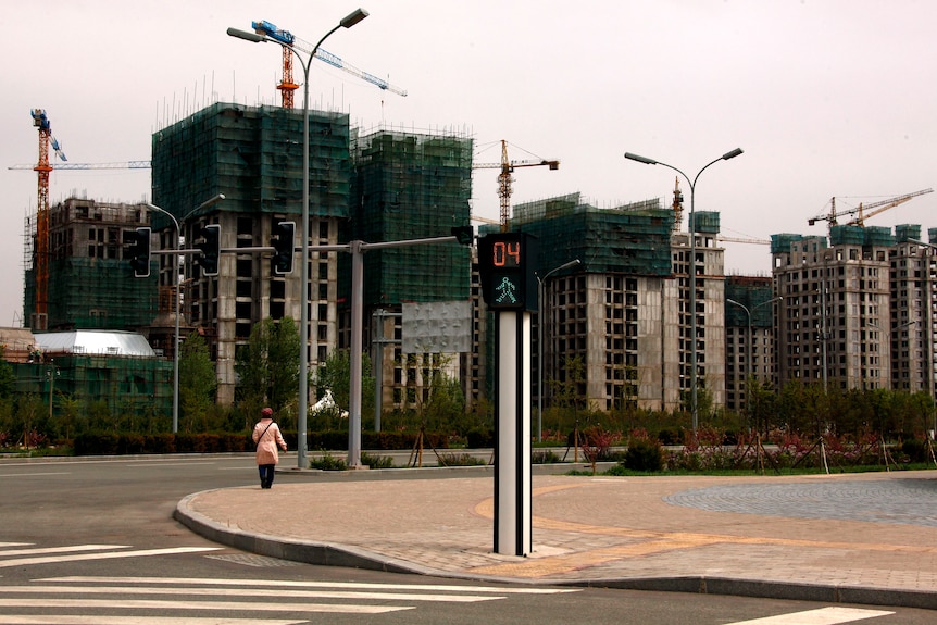 Una mujer camina por la acera de una calle vacía frente a las obras de construcción de edificios residenciales en el distrito Kangbashi de la ciudad de Ordos, Región Autónoma de Mongolia Interior, China