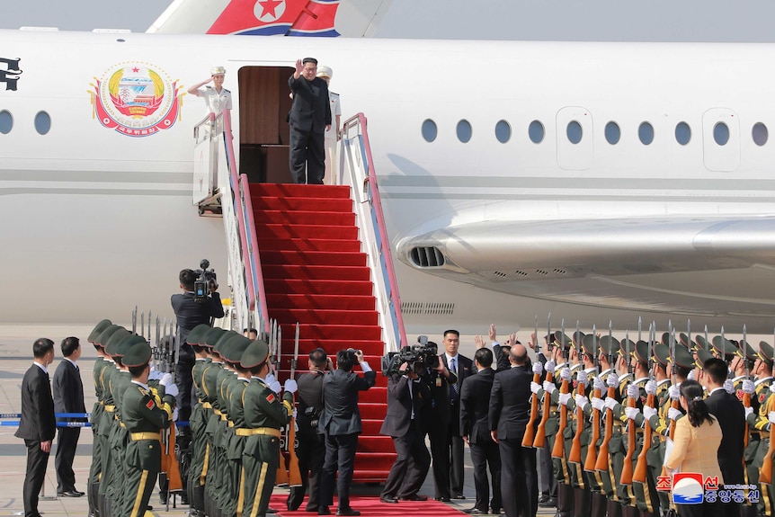 Kim Jong Un saluda mientras se prepara para descender los escalones cubiertos de alfombra roja de un avión.