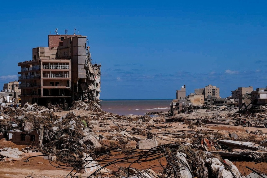 Edificios destruidos y suelo cubierto de escombros con el océano apareciendo detrás de ellos.