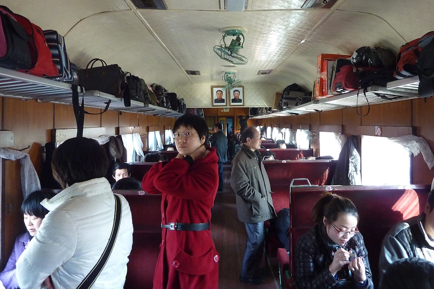 Los pasajeros se sientan y se paran en un tren mientras se ven las maletas en los estantes superiores.