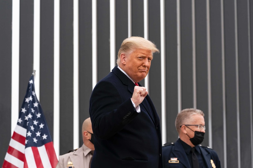 Donald Trump está parado frente a una pared mientras levanta el puño y sonríe.