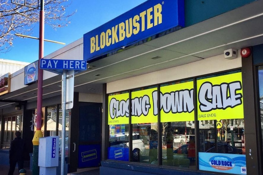 Una tienda de DVD Blockbuster con un cartel de venta cerrado en el frente.