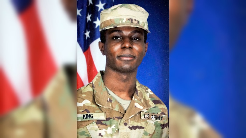 A photo of Travis King in army uniform, standing in front of an American flag. He is a black man  in his 20s with dark eyes.