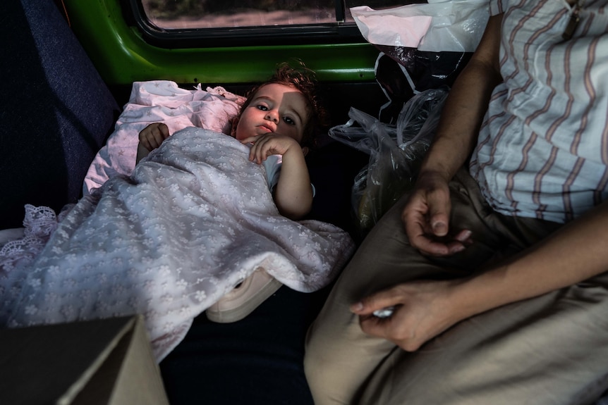 Un bebé con una manta enrollada está sentado en el asiento trasero de un coche.