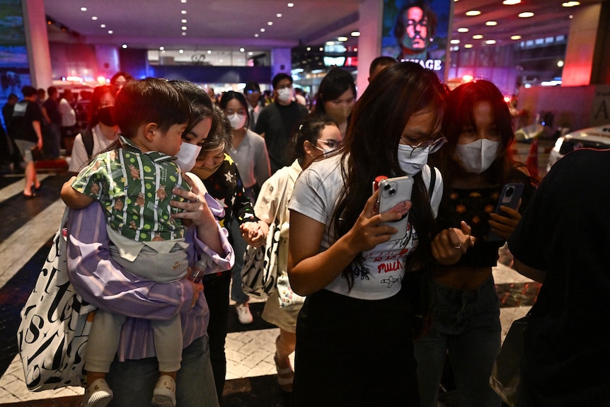 Una multitud de personas, en su mayoría mujeres, incluida una con un niño, saliendo corriendo de un centro comercial.