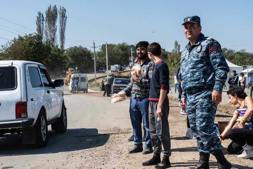 Un hombre está junto a un soldado que distribuye pan a los refugiados que pasan.