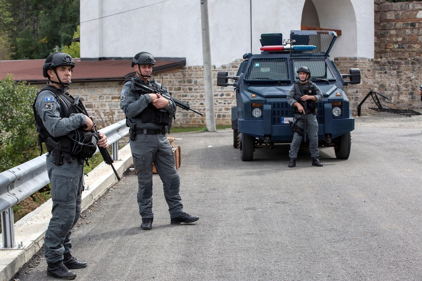 Tres policías fuertemente armados patrullan una calle en un vehículo blindado.