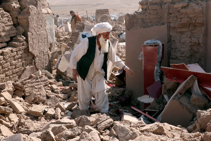 Un hombre parado entre los escombros después de un terremoto. 