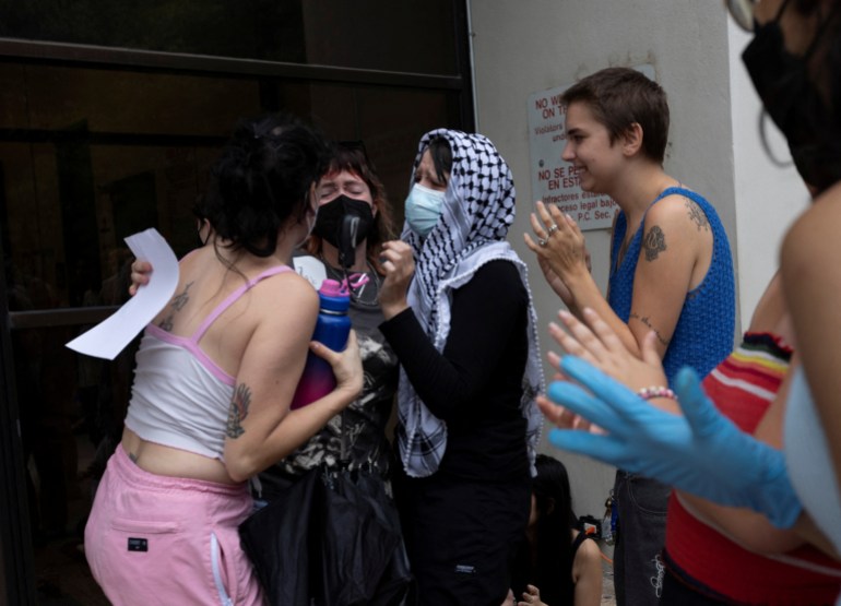 Los manifestantes se aplauden al salir de una cárcel de Austin.  Una mujer está rodeada de dos amigas que la abrazan, mientras sus ojos se cierran de emoción.