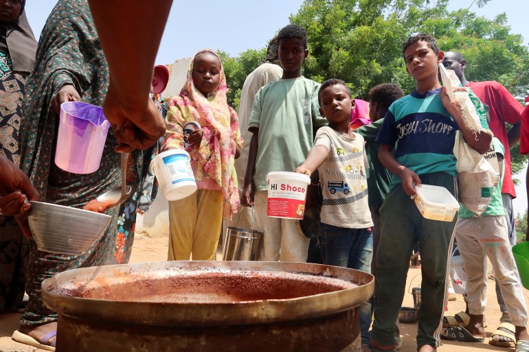 La gente sostiene ollas mientras los voluntarios distribuyen alimentos en Omdurman, Sudán, el 3 de septiembre de 2023.