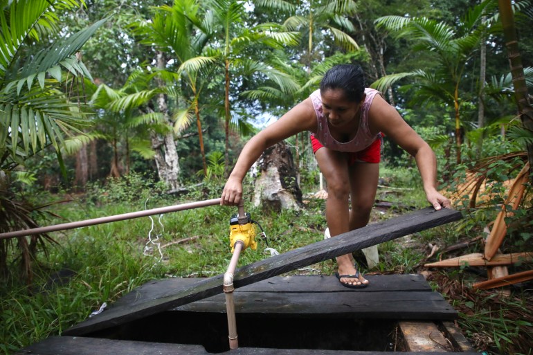 Una mujer se inclina para levantar tablas de madera sobre un pozo en la selva amazónica.