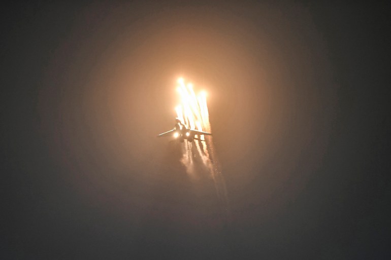 Un caza Sukhoi Su-30 participa en una exhibición aérea y emite bengalas que iluminan el cielo nocturno.