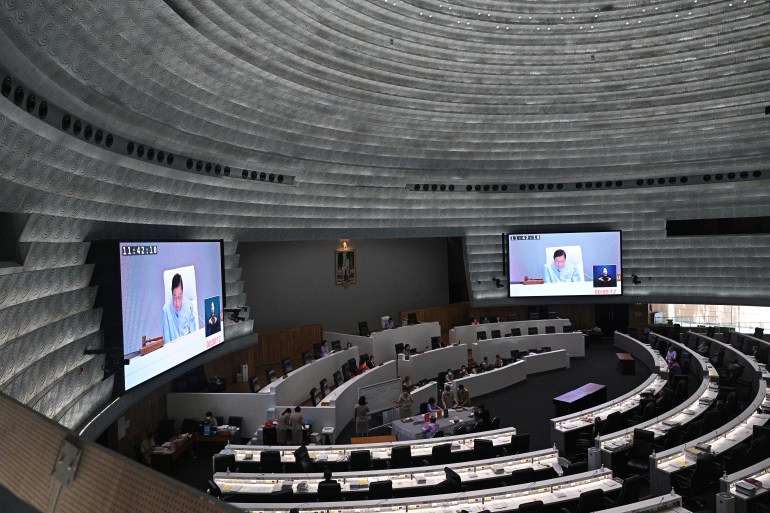 El interior del Senado tailandés en sesión.  Es gris.  Los asientos están dispuestos en semicírculo con dos pantallas gigantes delante a cada lado.