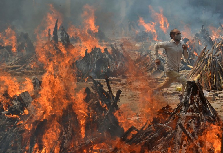 Un hombre corre para escapar del calor de varias piras funerarias de víctimas de COVID-19 en un crematorio en las afueras de Nueva Delhi, India, el 29 de abril de 2021. (Foto AP/Amit Sharma)