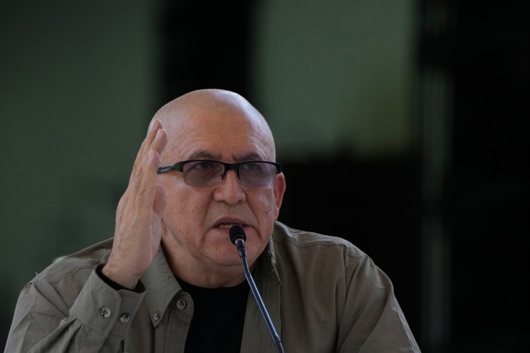 Antonio García, un hombre calvo con gafas de montura oscura y camisa verde oliva, hace gestos con las manos mientras habla por un micrófono.