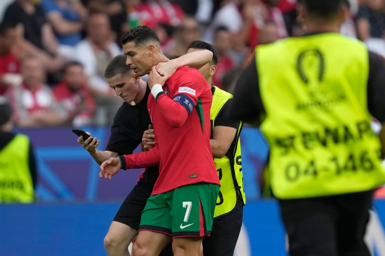 Un invasor del campo intenta tomarse una selfie con el portugués Cristiano Ronaldo mientras un camarero lo retira durante un partido del Grupo F entre Turquía y Portugal en el torneo de fútbol Euro 2024 en Dortmund, Alemania, el sábado 22 de junio de 2024. (Foto AP /Darko Vojinovic )