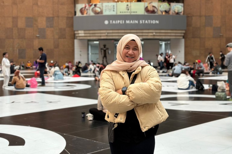 Anggi Sofiasyah Lacuba.  Está en la estación de Taipei.  Lleva una chaqueta con un pañuelo en la cabeza y tiene los brazos cruzados. 