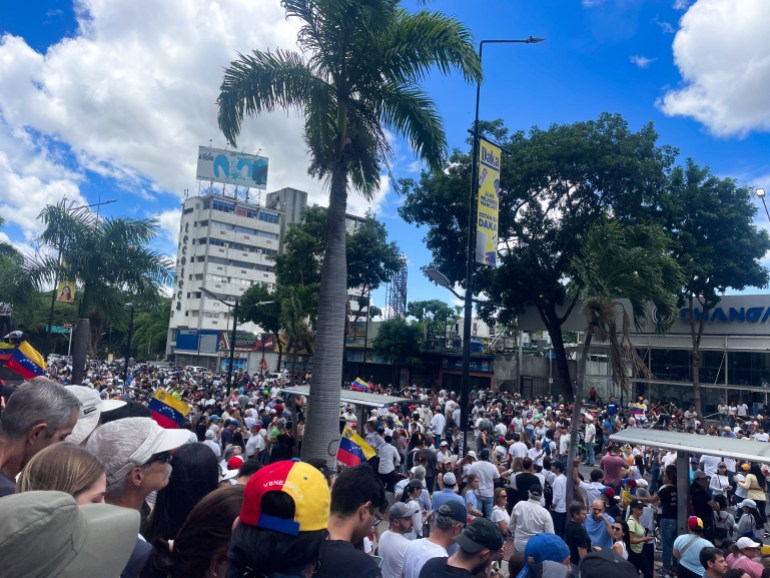 Multitudes se reúnen en una plaza abierta en Caracas, donde se ven palmeras y rascacielos.